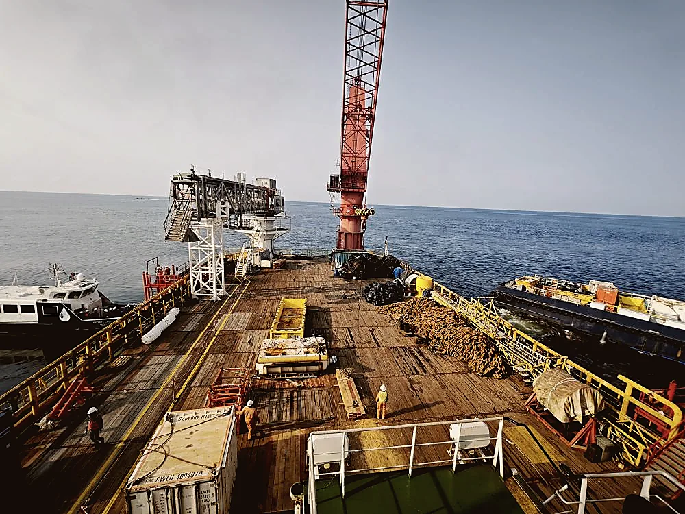 Barge deck with red pedestal crane and PPE workers