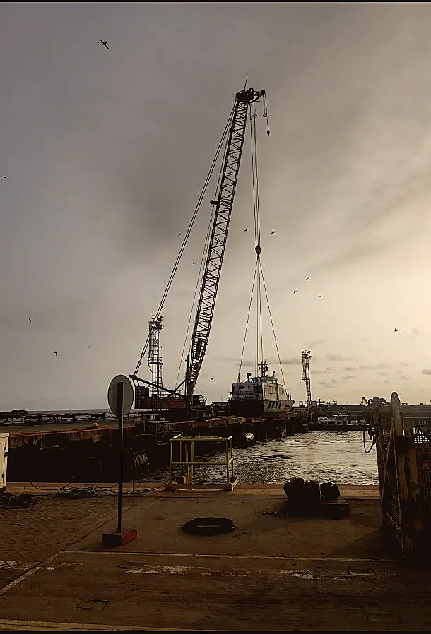 Pier crane loading supply vessel at dusk